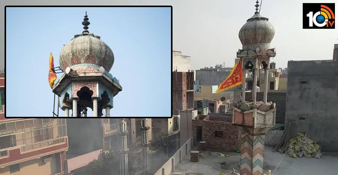 Men marching on top of a mosque, vandalising it and placing a saffron flag over it