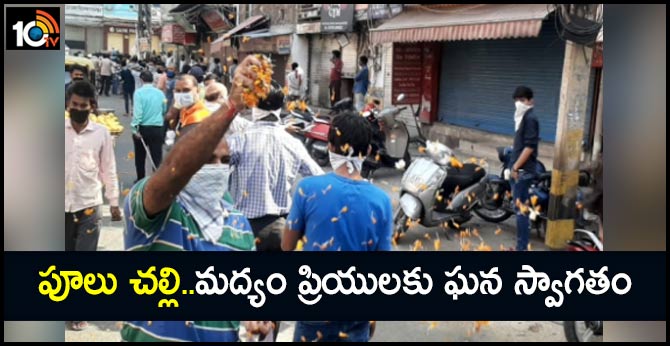 A man showers flower petals on people standing in queue outside liquor shops